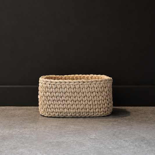 A small rectangular woven basket made of natural beige raffia or seagrass, placed on a gray stone floor against a dark charcoal wall.